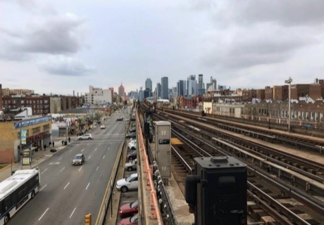 An elevated subway line over a Queens avenue, with the Manhattan skyline in the distance